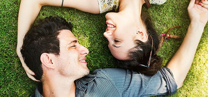 Amore incondizionato significato Amore incondizionato significato-fidanzati sdraiati sul prato in senso opposto uno all'altro si guardano negli occhi sorridendo