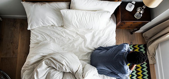 Come dimenticare una persona Come dimenticare una persona-vista dall’alto di ragazzo seduto sul letto che pensa guardando nel vuoto con volto appoggiato sulle mani