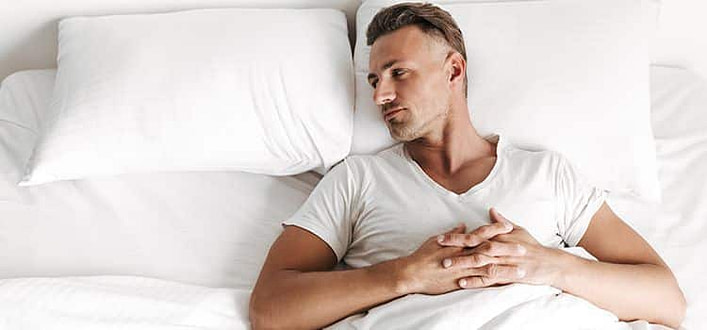 Soffrire per amore Soffrire per amore-ragazzo pensieroso sveglio nel letto sotto lenzuola bianche con testa girata di profilo sul cuscino bianco