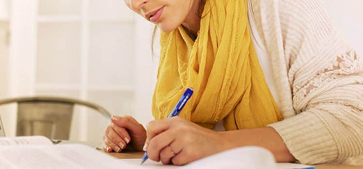 Frasi sulla coerenza Frasi sulla coerenza-donna con foulard giallo che scrive su un foglio appoggiata sul tavolo di un ambiento domestico
