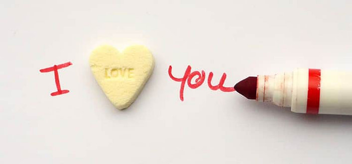 Ti voglio bene o ti amo i voglio bene o ti amo-pennarello rosso che completa la frase I love you dove love è già scritto su una caramella bianca a forma di cuore