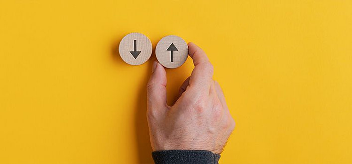 Frasi sulle scelte Frasi sulle scelte-pedine in legno su sfondo giallo con frecce in basso e in alto e mano che spinge pedina con freccia in alto