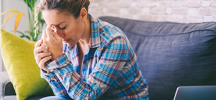 ansia generalizzata ansia generalizzata-donna pensierosa con camicia a scacchi seduta sul divano con occhi chiusi e fronte appoggiata alle mani