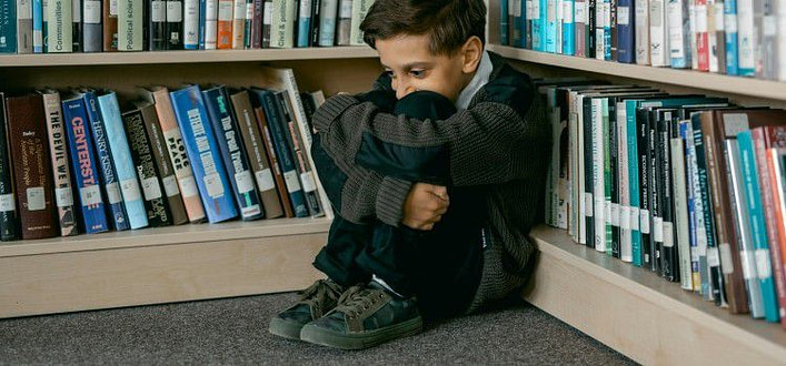 I libri da leggere-bambino seduto a terra rannicchiato nell'angolo di una liberaria I libri da leggere-bambino seduto a terra rannicchiato nell'angolo di una liberaria