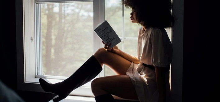 Libri belli da leggere-donna seduta di profilo alla finestra legge libro appoggiato sulle gambe Libri belli da leggere-donna seduta di profilo alla finestra legge libro appoggiato sulle gambe
