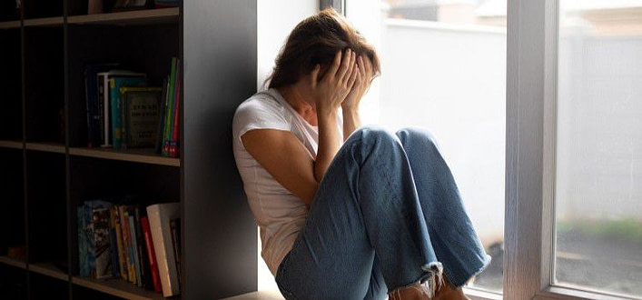 Definizione ossessione-ragazza rannicchiata a terra davanti a finestra con mani sul volto a coprire gli occhi Definizione ossessione-ragazza rannicchiata a terra davanti a finestra con mani sul volto a coprire gli occhi