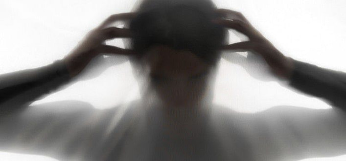 Immagine sfuocata di persona con mani aperte e dita a comprimere le tempie Immagine sfuocata di persona con mani aperte e dita a comprimere le tempie