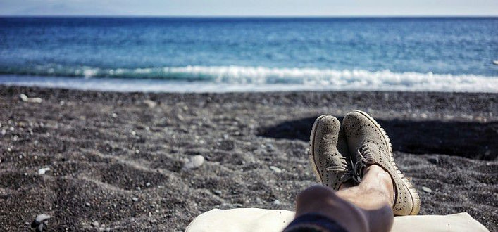 Primo piano delle gambe di un uomo distese su lettino da spiaggia con piedi incrociati davanti al mare Primo piano delle gambe di un uomo distese su lettino da spiaggia con piedi incrociati davanti al mare