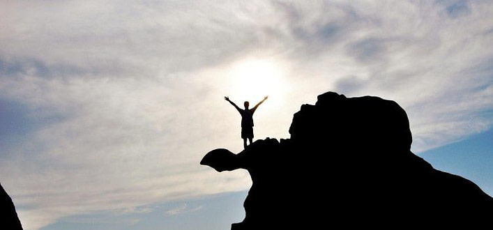 silhouette di uomo con braccia aperte su roccia a sbalzo e cielo nuvoloso sullo sfondo silhouette di uomo con braccia aperte su roccia a sbalzo e cielo nuvoloso sullo sfondo