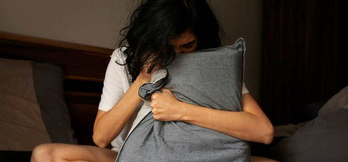Calmare un attacco di panico - ragazza affranta seduta sul letto stringendo un cuscino Calmare un attacco di panico - ragazza affranta seduta sul letto stringendo un cuscino