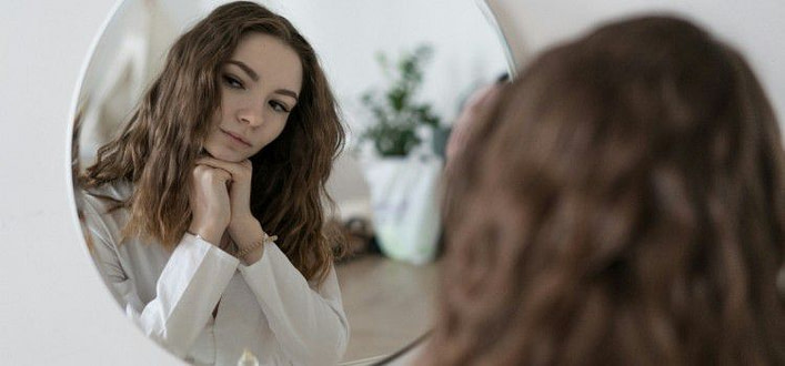 Profezia che si autoavvera-ragazza di spalle che si riflette nello specchio tondo sulla parete Profezia che si autoavvera-ragazza di spalle che si riflette nello specchio tondo sulla parete