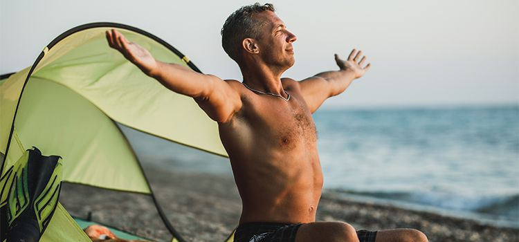stare bene da soli-ragazzo seduto in spiaggia che sorride a braccia aperte