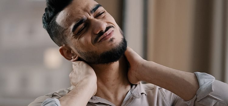 Ansia e dolori muscolari-ragazzo con smorfia sul viso e mani sul collo dolente