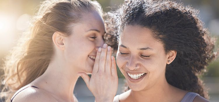 Il segreto per essere felici - Una ragazza sorridente parla all'orecchio di un'altra ragazza sorridente