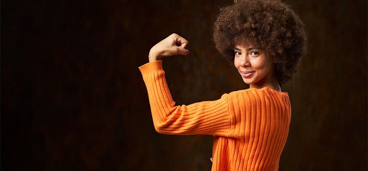 come essere forte - Ragazza sorridente su sfondo nero che mostra il bicipite in segno di forza