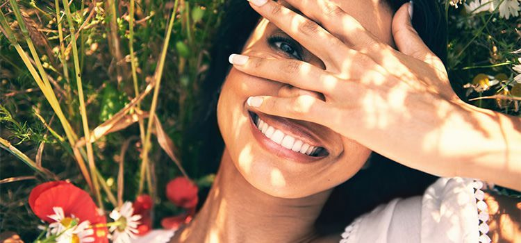 Il segreto della felicità - donna sorridente che copre il visto con la mano lasciando intravedere l'occhio sinistro