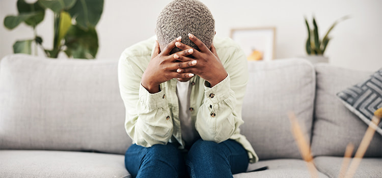 per quale motivo viene l'ansia - donna seduta su un divano piegata in avanti con le mani sulla testa