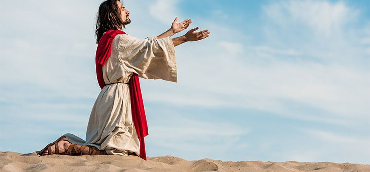 Gesù nel deserto - Un uomo vestito come Gesù prega nel deserto in ginocchio