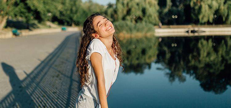 come combattere lo stress - una ragazza sorridente e rilassata sulle sponde di un fiume