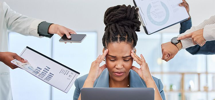 come ridurre lo stress - una donna che si tiene le tempi con le mani mentre tutti le chiedono qualche cosa.