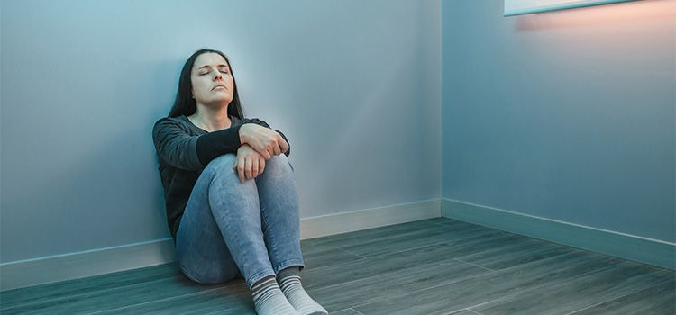 mi manca qualcosa - Ragazza seduta a terra e appoggiata a un muro in una stanza vuota