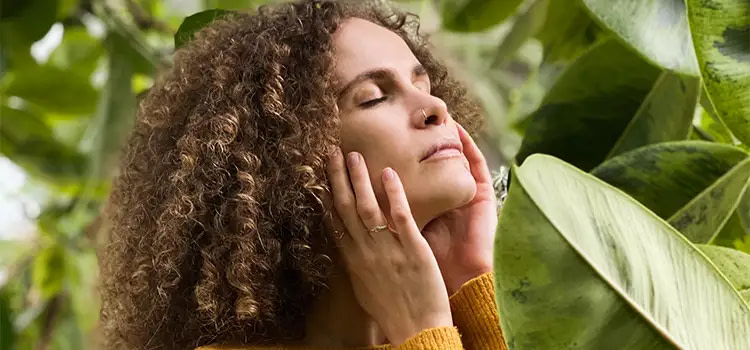 Come curare l'ansia in modo naturale - Donna che si rilassa con gli occhi chiusi in mezzo a delle piante verdi