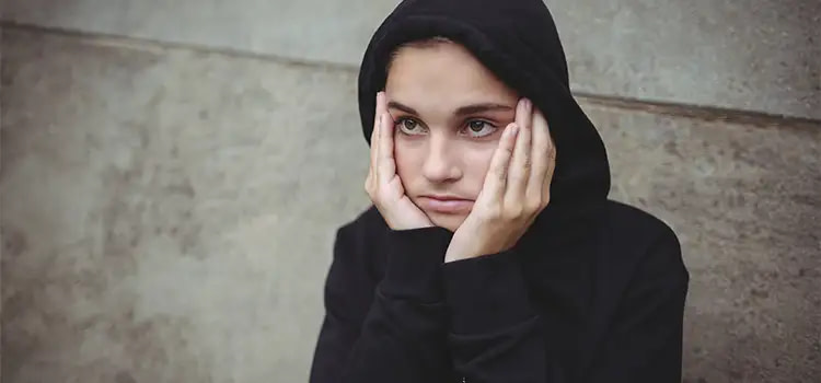 emozioni tristi - un ragazzo con un cappuccio ha le mani lungo i lati del volto
