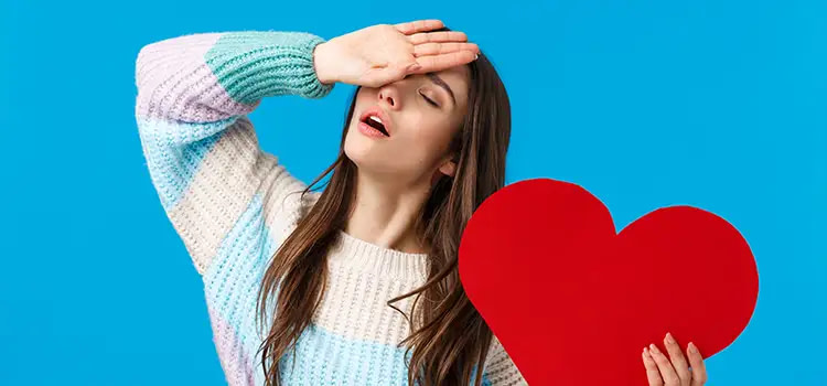 Ragazza che mima di soffrire con un cuore di cartone rosso in mano